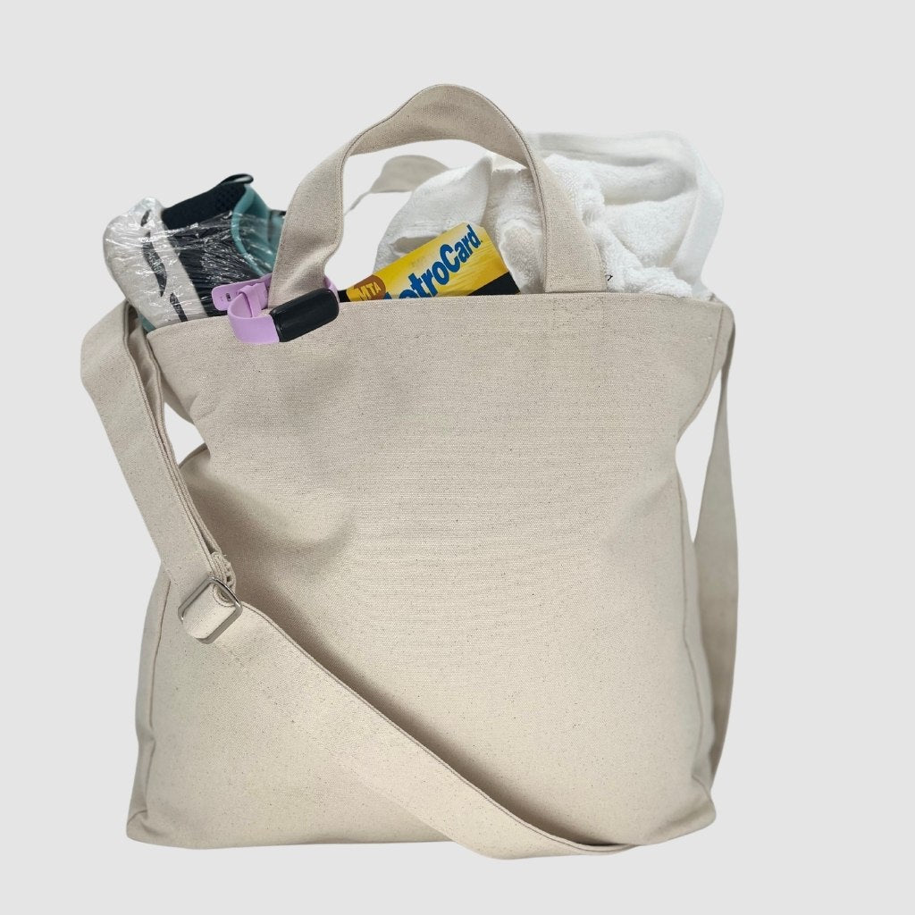 Reusable crossbody canvas bag filled with everyday essentials such as a towel, MetroCard, and water bottle, showcasing its spaciousness and practicality.