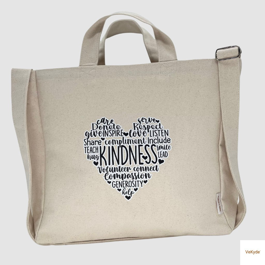 Natural canvas crossbody grocery bag with heart-shaped “Kindness” word art print, featuring adjustable strap and durable design